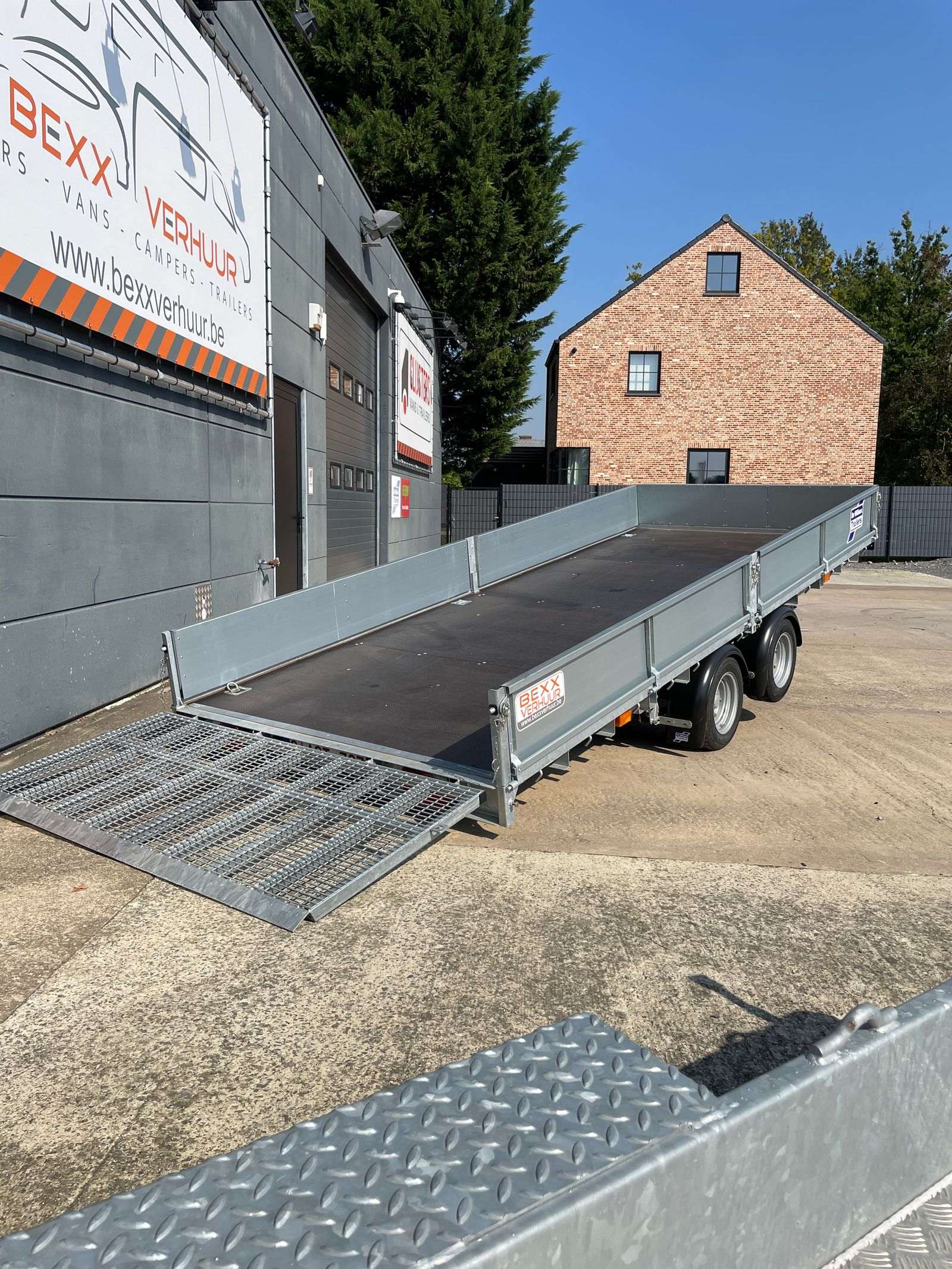 De trailer met de zijborden op en de oprijplaat neer, aan de loods